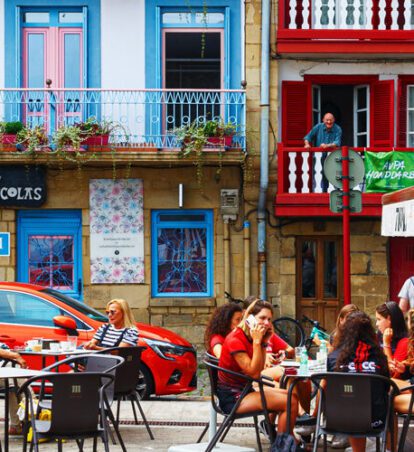 an outdoor patio full of people with colorful buildings in the background